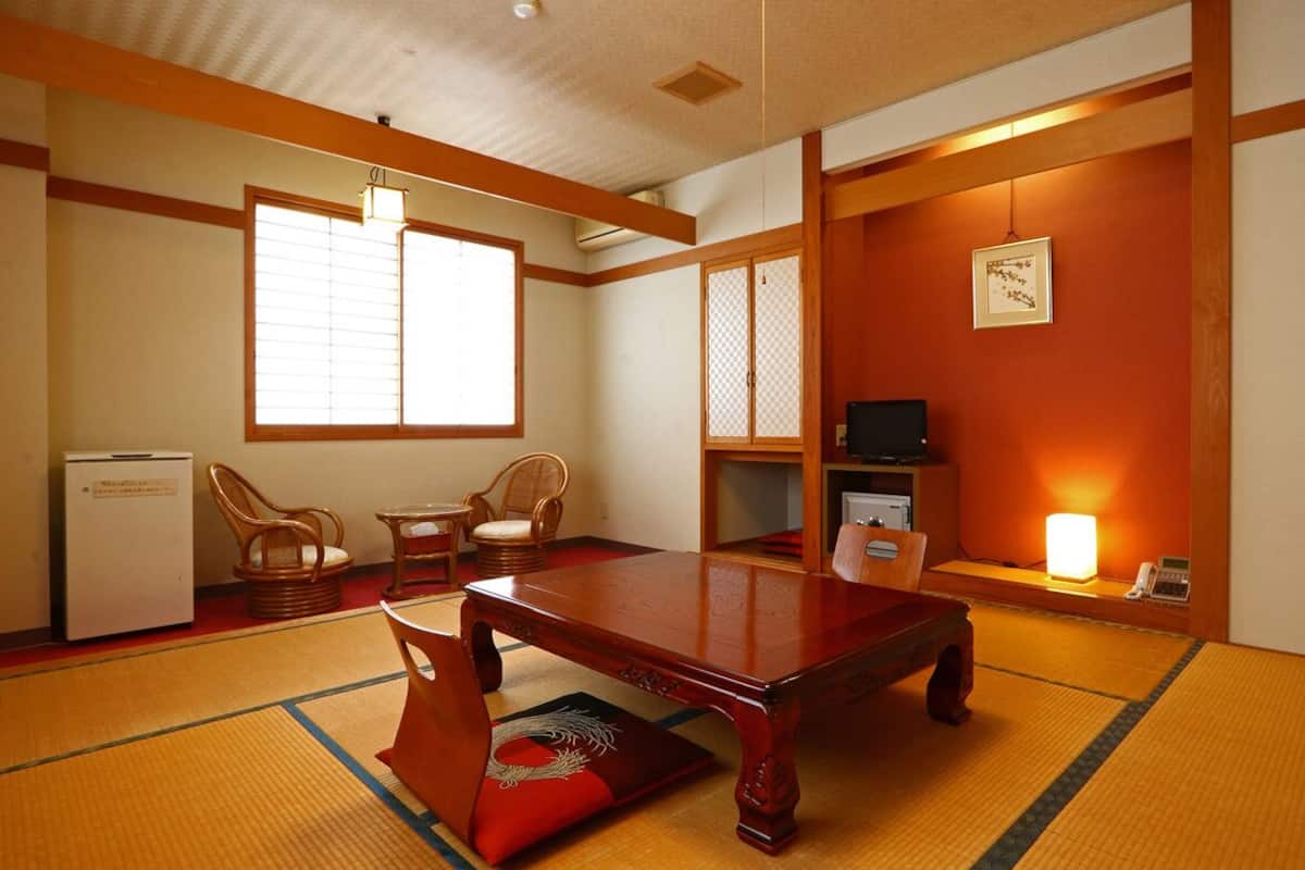 A traditional Japanese room with tatami flooring, a low table, two chairs, a television, and a refrigerator.