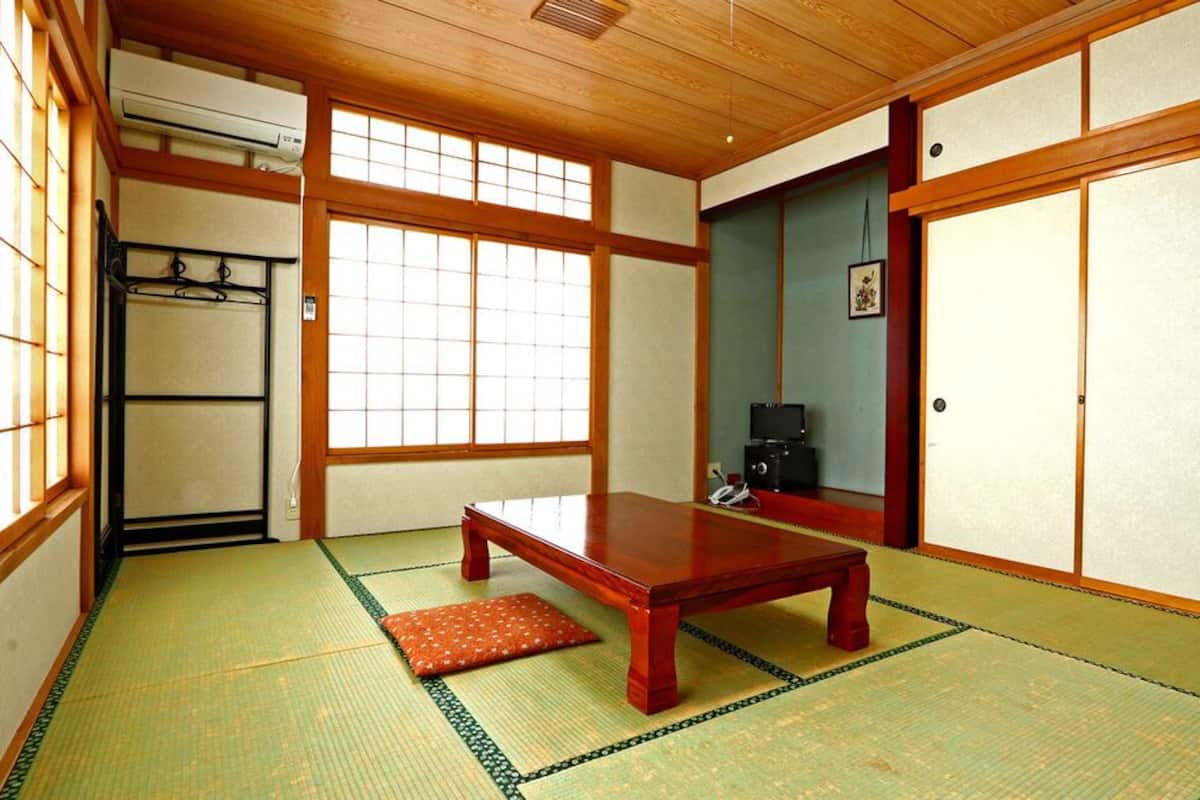 A traditional Japanese room with tatami flooring, a low wooden table, sliding doors, and a television.