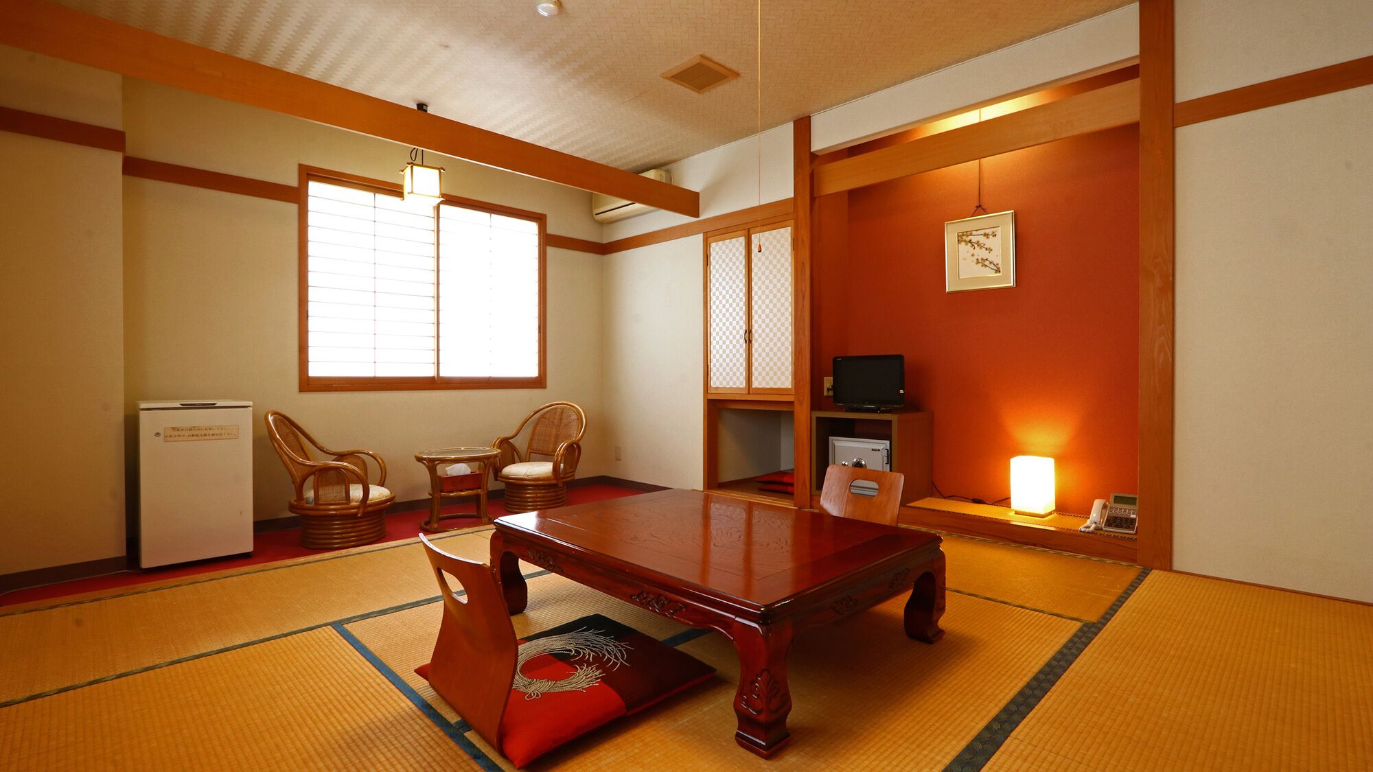 A traditional Japanese room with tatami flooring, a low table, two chairs, a television, and a small refrigerator.
