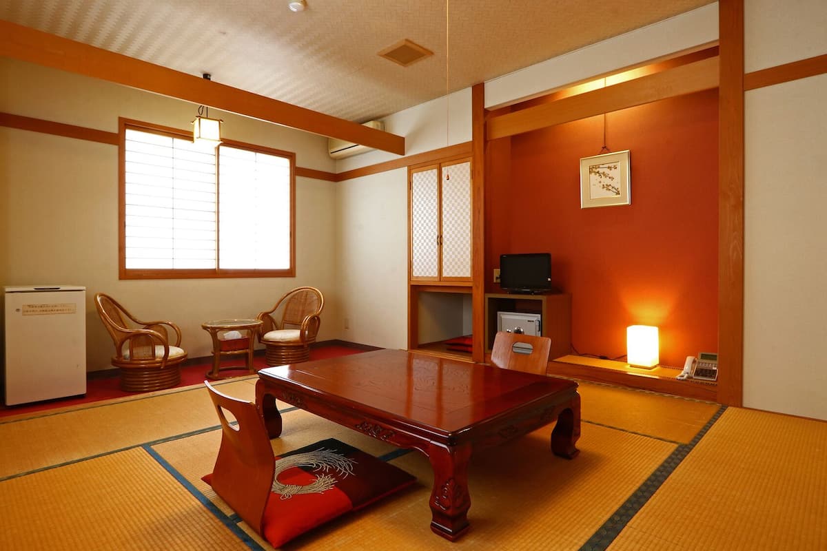 A traditional Japanese room with tatami flooring, a low table, two chairs, a television, and a small refrigerator.