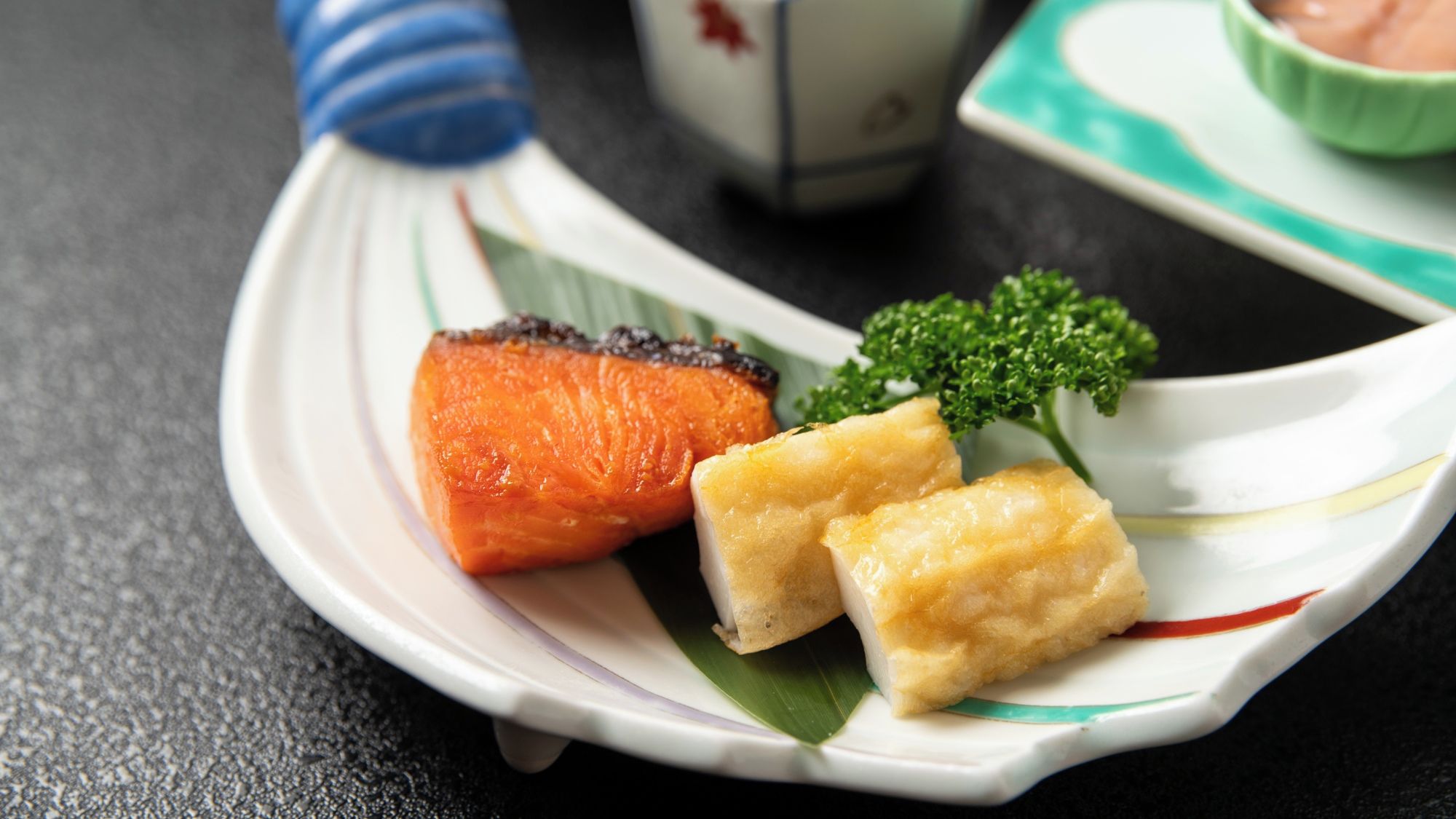 A plate with grilled salmon, a piece of tofu, and a garnish of green herbs.