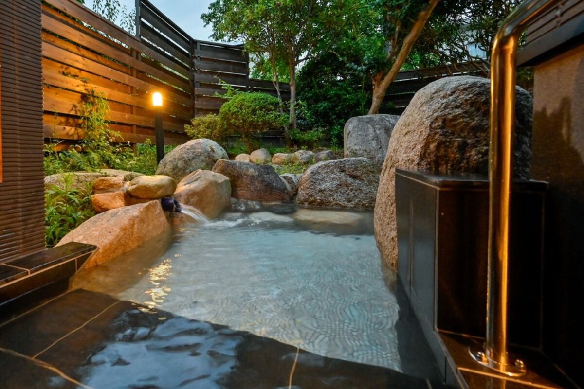 A spa area with a hot spring, large rocks, and a wooden fence.