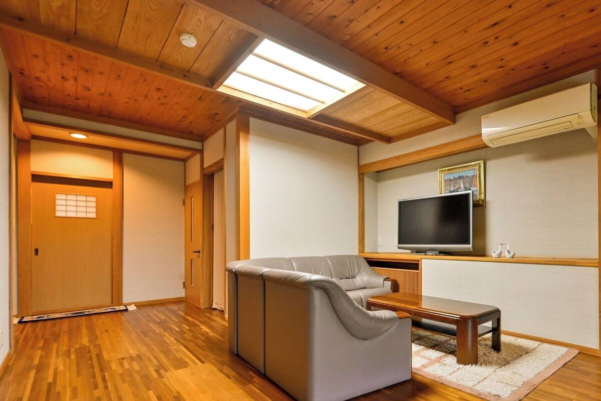 A room with a sofa, a television, a wooden ceiling, and a sliding door.