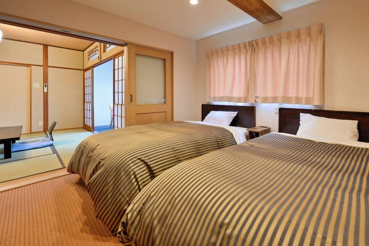 A hotel room with two beds, a wooden headboard, a small bedside table, a chair, and a sliding door leading to a bathroom.