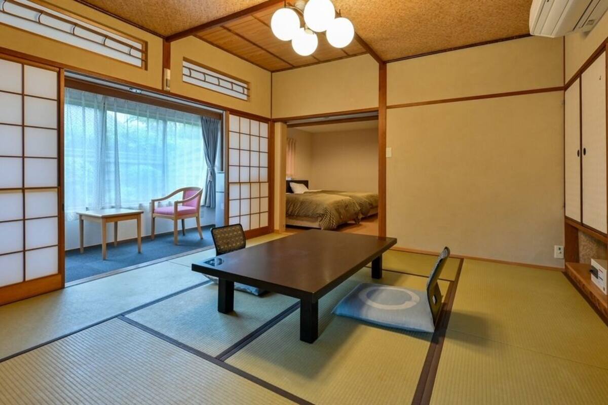 A traditional Japanese room with tatami flooring, a low table, a chair, and sliding doors leading to another room.