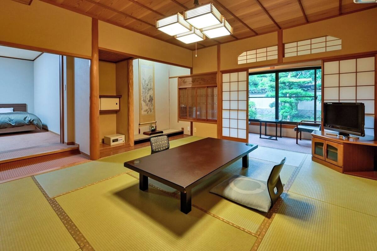 A traditional Japanese room with tatami flooring, a low table, a bed, a TV, and sliding doors.