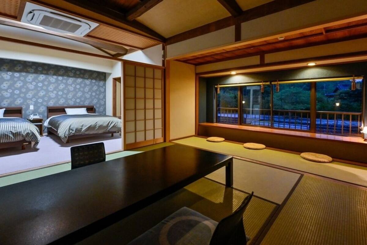 A traditional Japanese-style room with tatami flooring, two beds with striped bedding, a low table, and a window with a view of the outside.