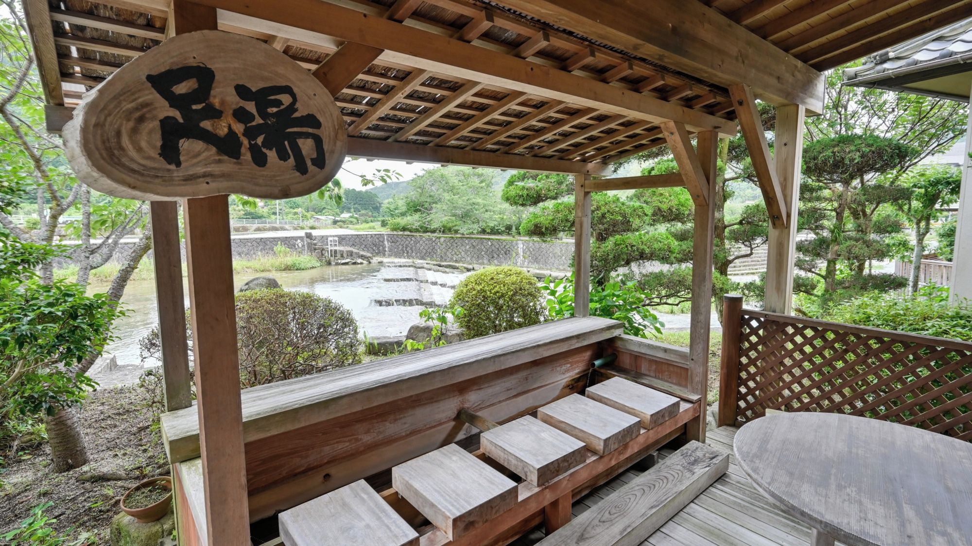 A wooden deck with benches overlooking a garden and a stone bridge.