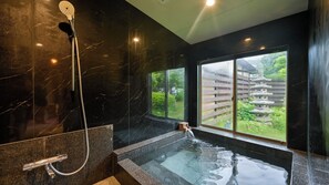 A modern bathroom with a marble wall, a shower, a bathtub, and a view of a traditional Japanese garden.