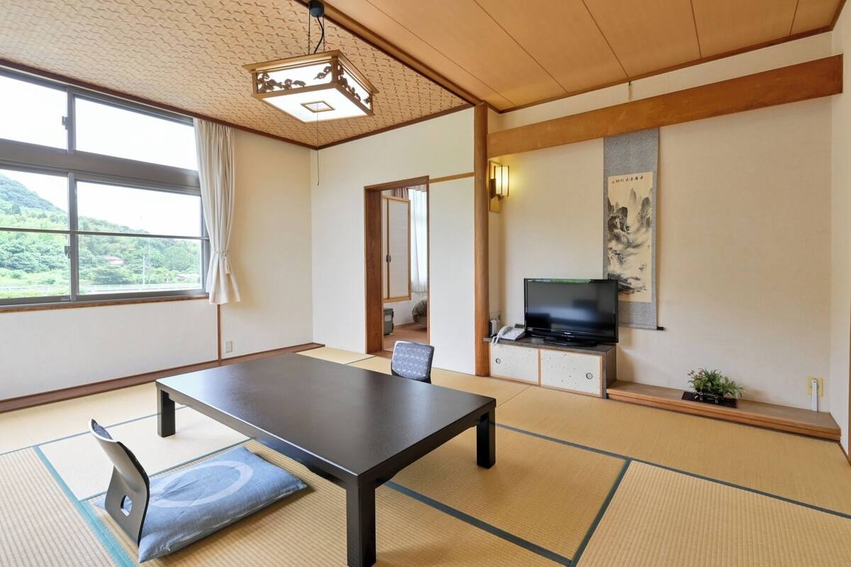 A traditional Japanese-style room with tatami flooring, a low table, a television, and a painting on the wall.