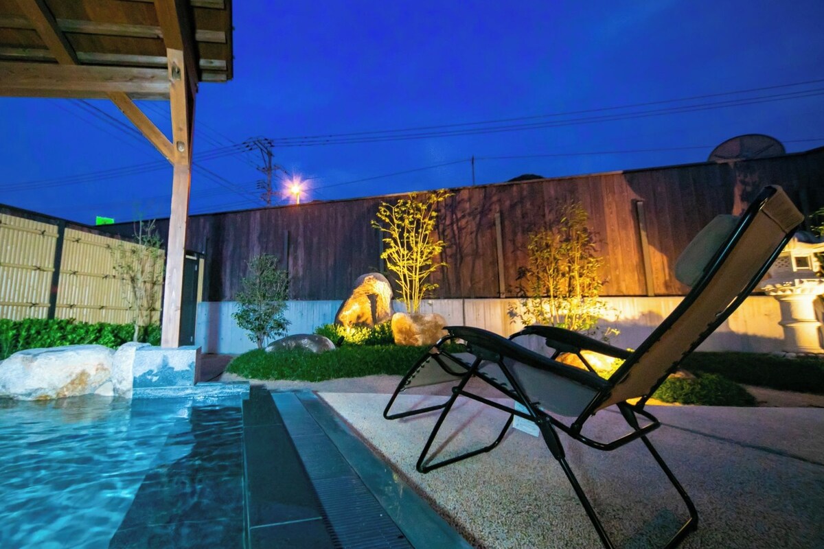 A swimming pool with a lounge chair, rocks, and a wooden fence.