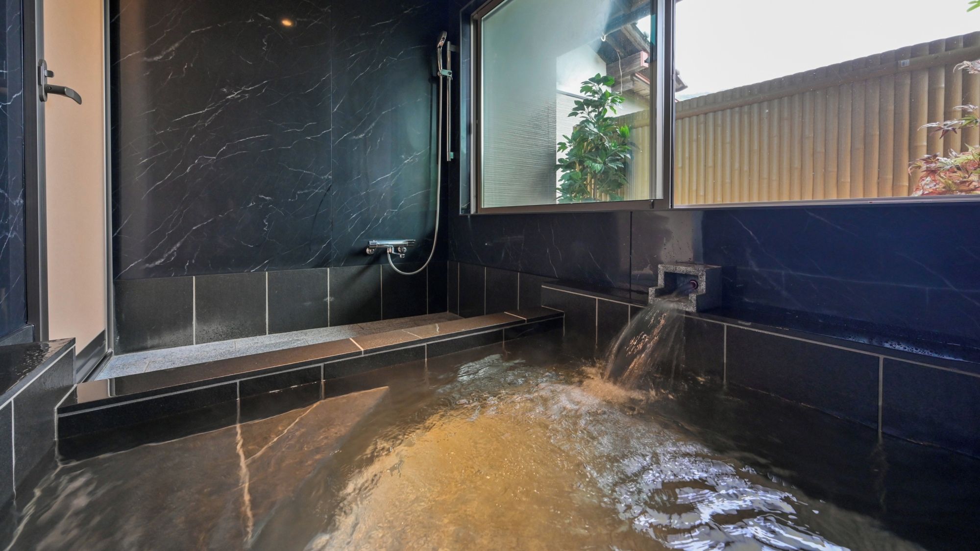 Une salle de bain moderne avec un mur en marbre, une douche et une baignoire où l’eau coule.