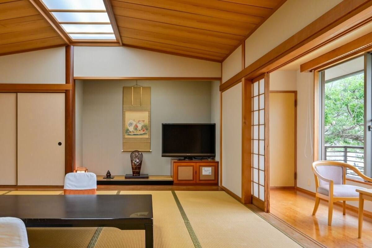 A traditional Japanese room with tatami flooring, a tatami mat table, a television, and sliding doors leading to a balcony.