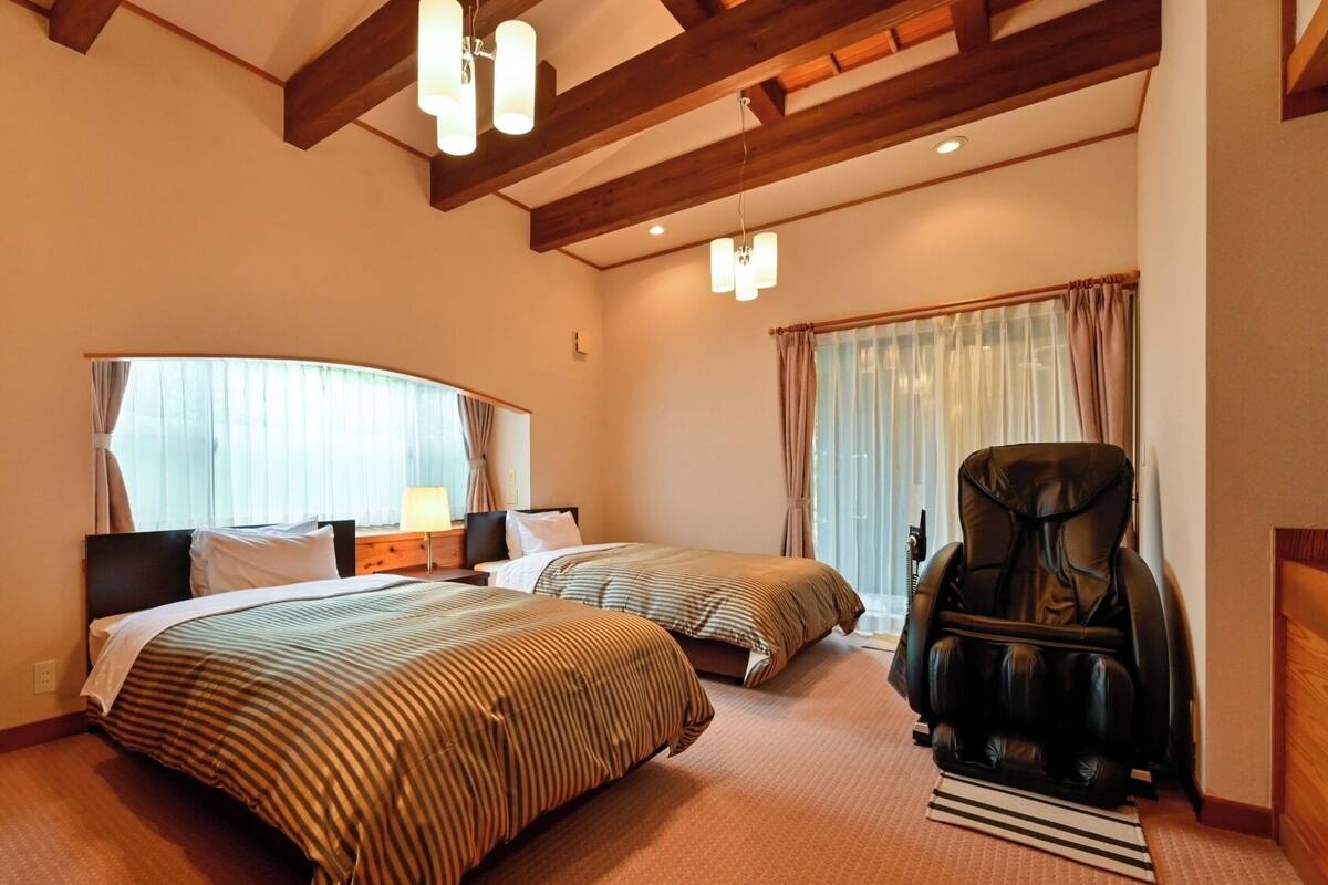 A hotel room with two beds, a massage chair, and a large window with curtains.