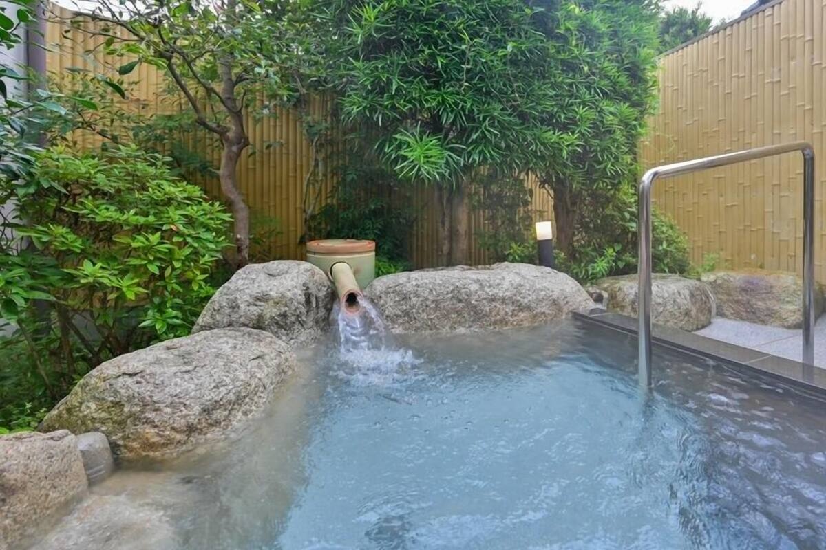 A hot spring area with a stone pool, rocks, and bamboo fencing.