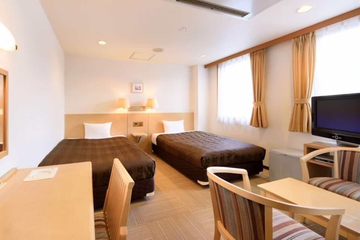 Une chambre d’hôtel avec deux lits, une télévision, un bureau et une chaise.