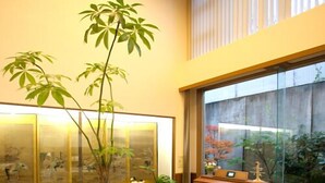 A modern living room with a piano, two potted plants, and a large window overlooking a garden.