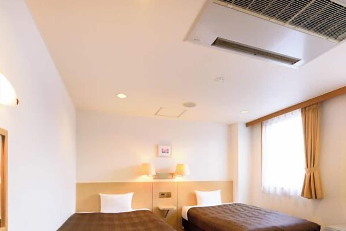 Une chambre d’hôtel avec deux lits, un bureau, une chaise, une fenêtre avec des rideaux et un appareil de climatisation.