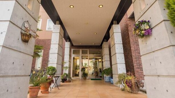 A covered walkway with concrete pillars, potted plants, and a glass entrance.