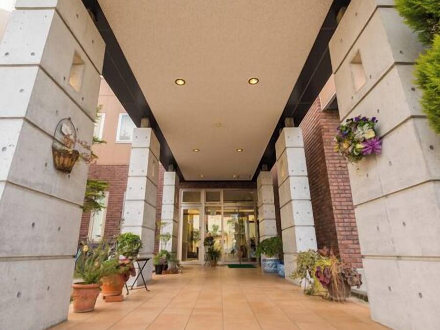 A covered walkway with concrete pillars, potted plants, and a glass entrance.