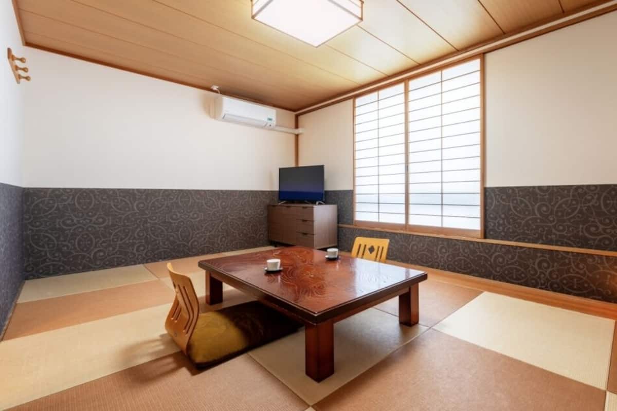 Une pièce de style japonais traditionnel, avec un sol recouvert de tatamis, une petite table en bois, un téléviseur et un paravent en papier de riz (shoji).