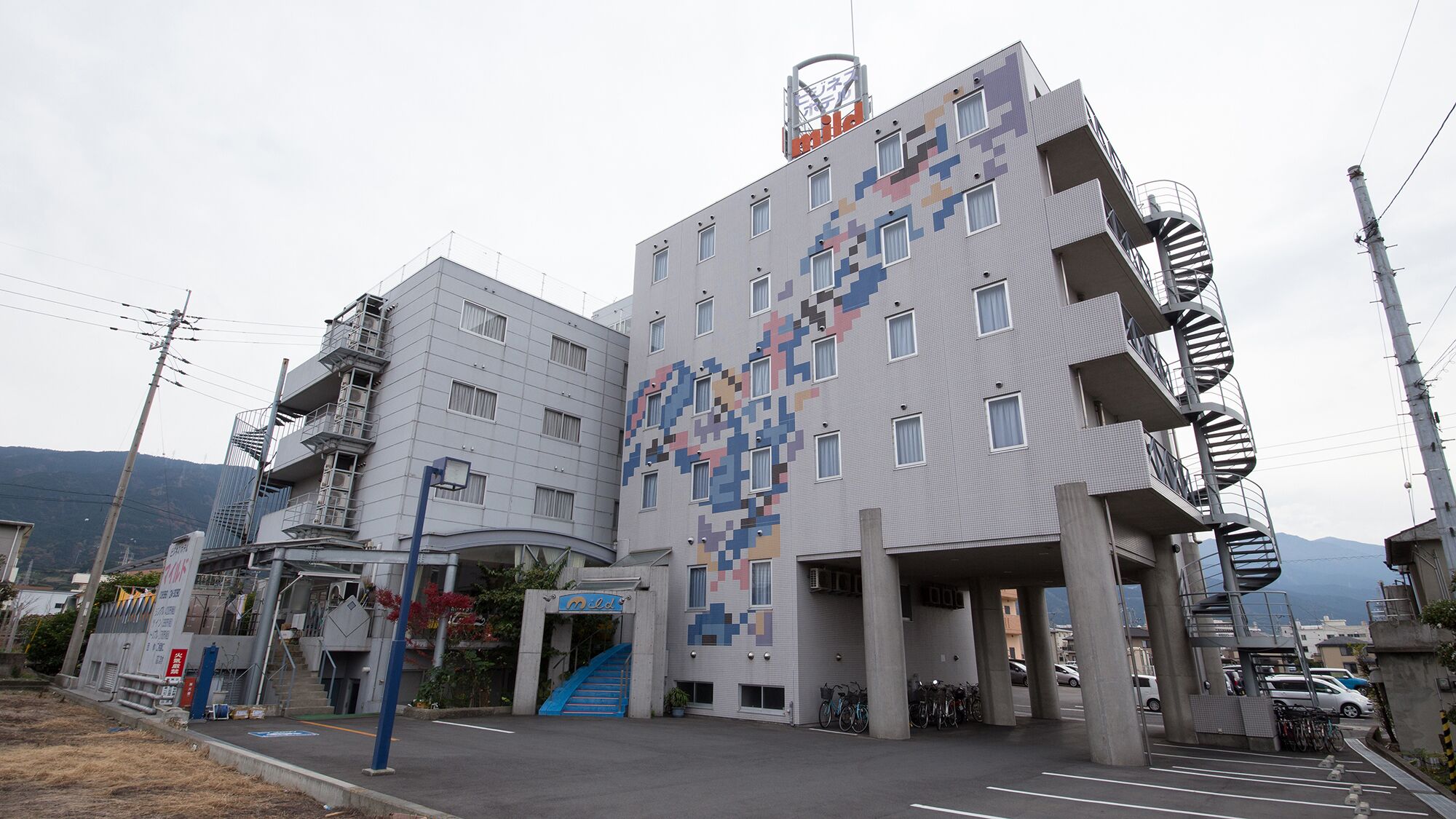 Um edifício moderno com fachada pixelizada única, entrada azul e uma escadaria em espiral à direita.