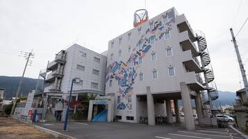 Um edifício moderno com fachada pixelizada única, entrada azul e uma escadaria em espiral à direita.