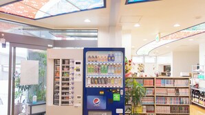 Una macchina distributrice con diverse bevande e snack, una libreria con libri e l'ingresso con una porta in vetro.