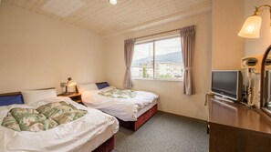 Habitación de hotel con dos camas, televisor, escritorio y ventana con vistas a edificios y montañas.