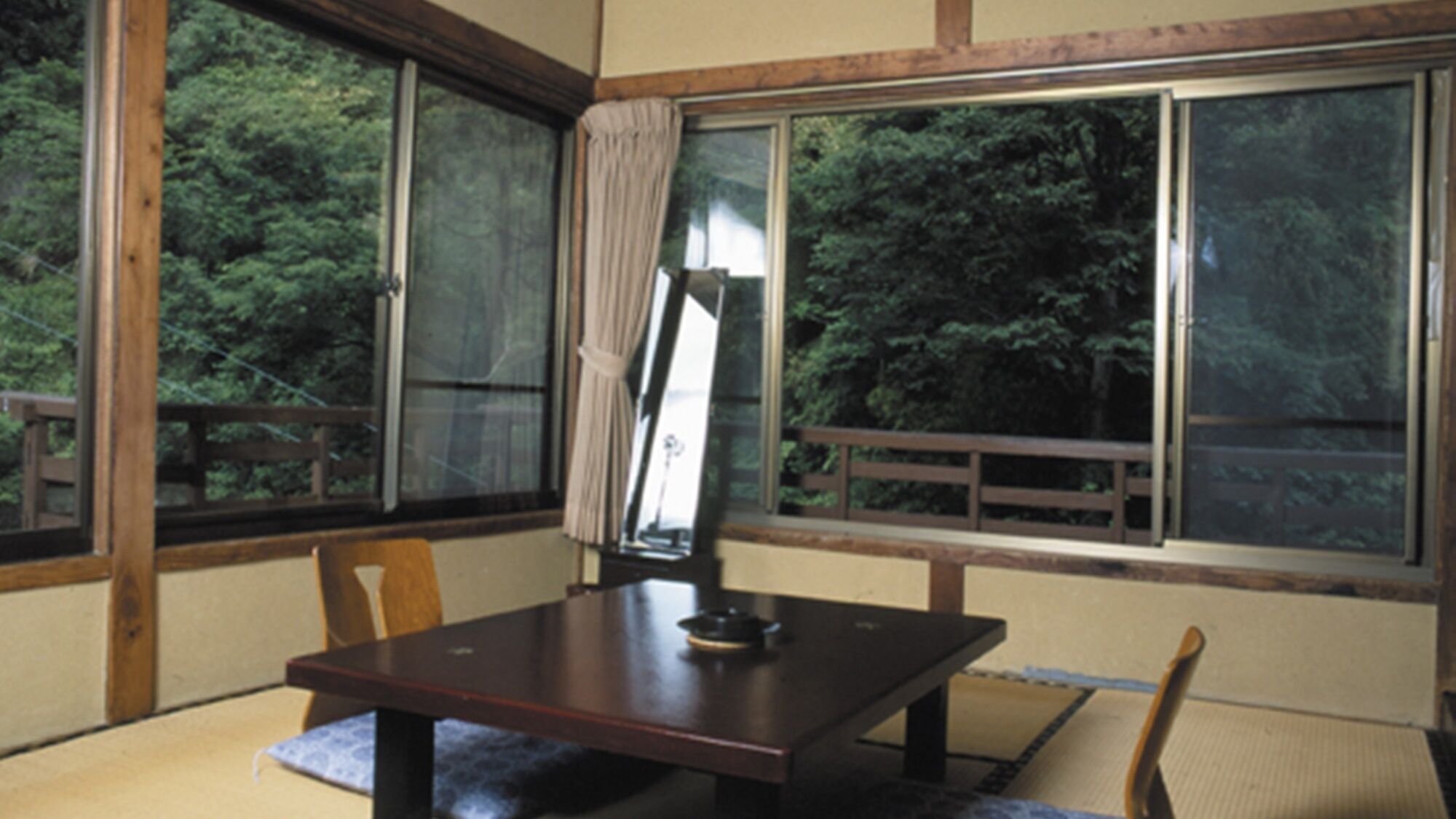 A room with a wooden table, chairs, and large windows offering a view of trees.