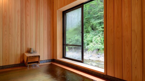 Una habitación con paredes de madera, un ventanal grande, una mesita de madera y un banco.