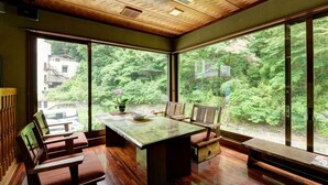 Una habitación con una mesa grande y sillas, ventanas amplias con vista a un bosque y techo de madera.