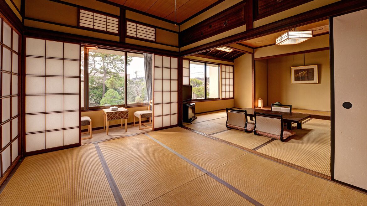 Una habitación japonesa tradicional con suelo de tatami, puertas correderas, una mesa baja con cojines y un televisor.