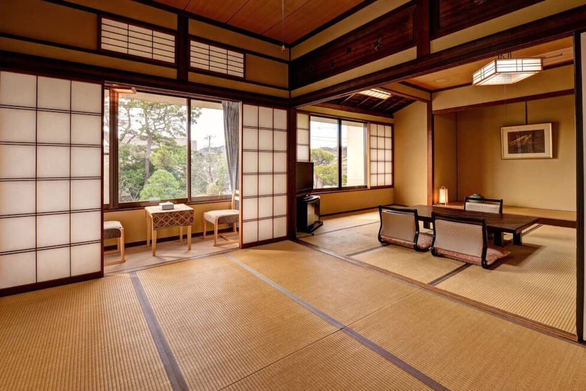 Una habitación japonesa tradicional con suelo de tatami, puertas correderas, una mesa baja con cojines y un televisor.
