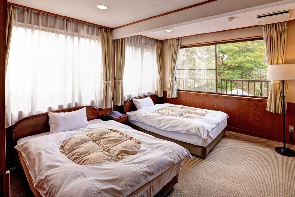 Una habitación de hotel con dos camas, una ventana con vistas, una lámpara y suelo de madera.