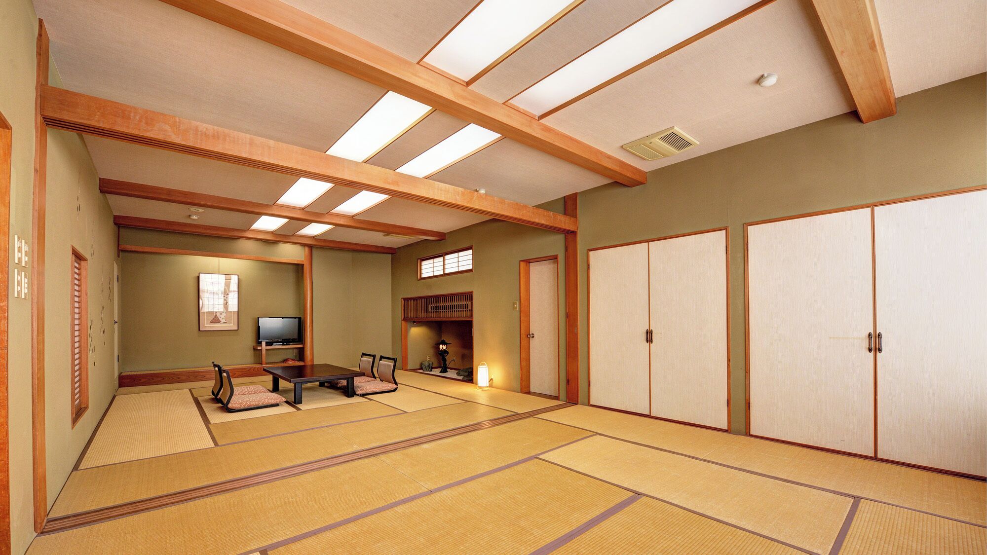 Una habitación tradicional japonesa con suelo de tatami, televisor, una mesa baja de tatami y puertas correderas.