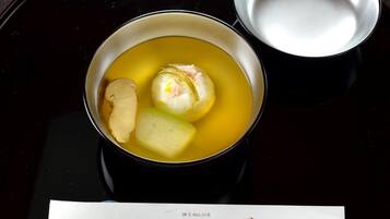 A bowl of soup with dumplings and slices of fish on a black tray.