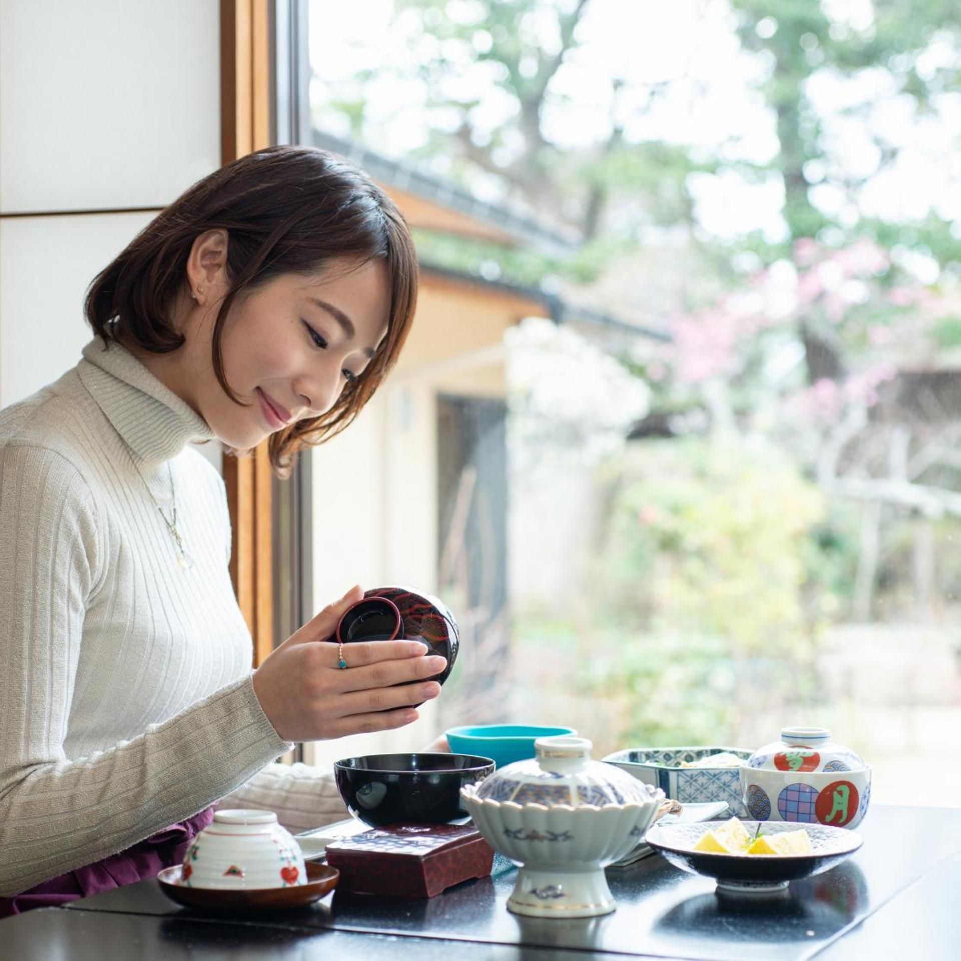 A person holding a cup, seated at a table with various bowls and dishes.