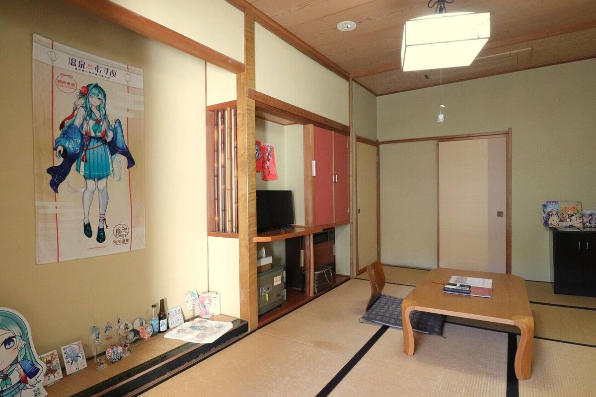 Habitación japonesa tradicional con suelo de tatami, una mesa baja de tatami, un televisor y un cartel en la pared.