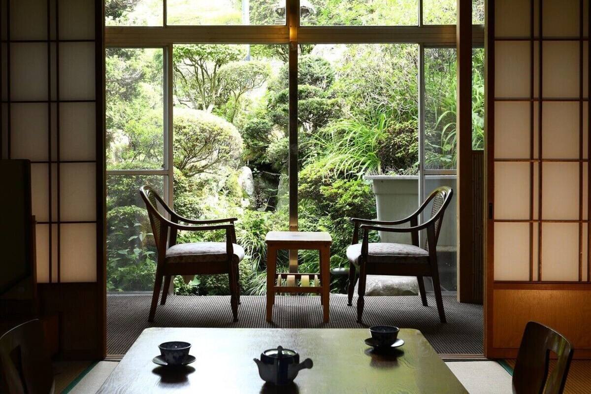 Una habitación japonesa tradicional con suelo de tatami, una mesita baja con juego de té y vistas a un exuberante jardín a través de grandes puertas correderas.