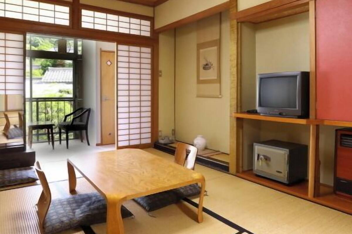 Una habitación japonesa tradicional con suelo de tatami, una mesa baja y un televisor en un estante.