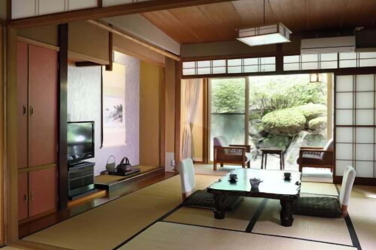 Una habitación japonesa tradicional con suelo de tatami, una mesa baja con cojines, puertas correderas y vistas al verde exterior.