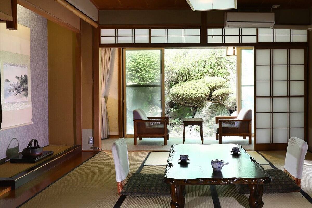 Una habitación japonesa tradicional con suelo de tatami, un puertas correderas que dan a un jardín y una mesa baja con un juego de té.
