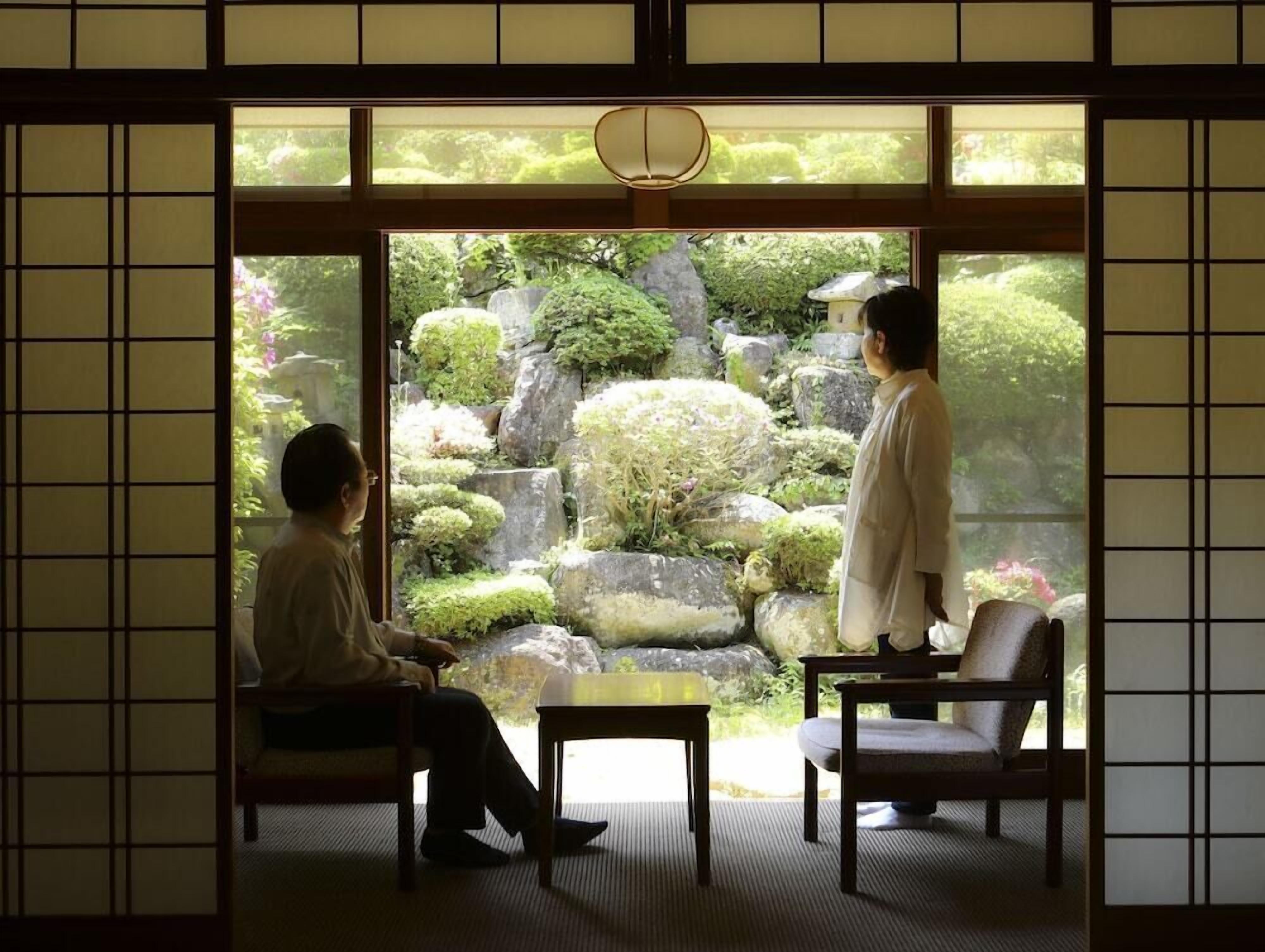 A traditional Japanese room with tatami flooring, a low table, and a view of a garden through a sliding door.