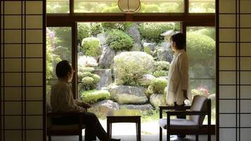 A traditional Japanese room with tatami flooring, a low table, and a view of a garden through a sliding door.