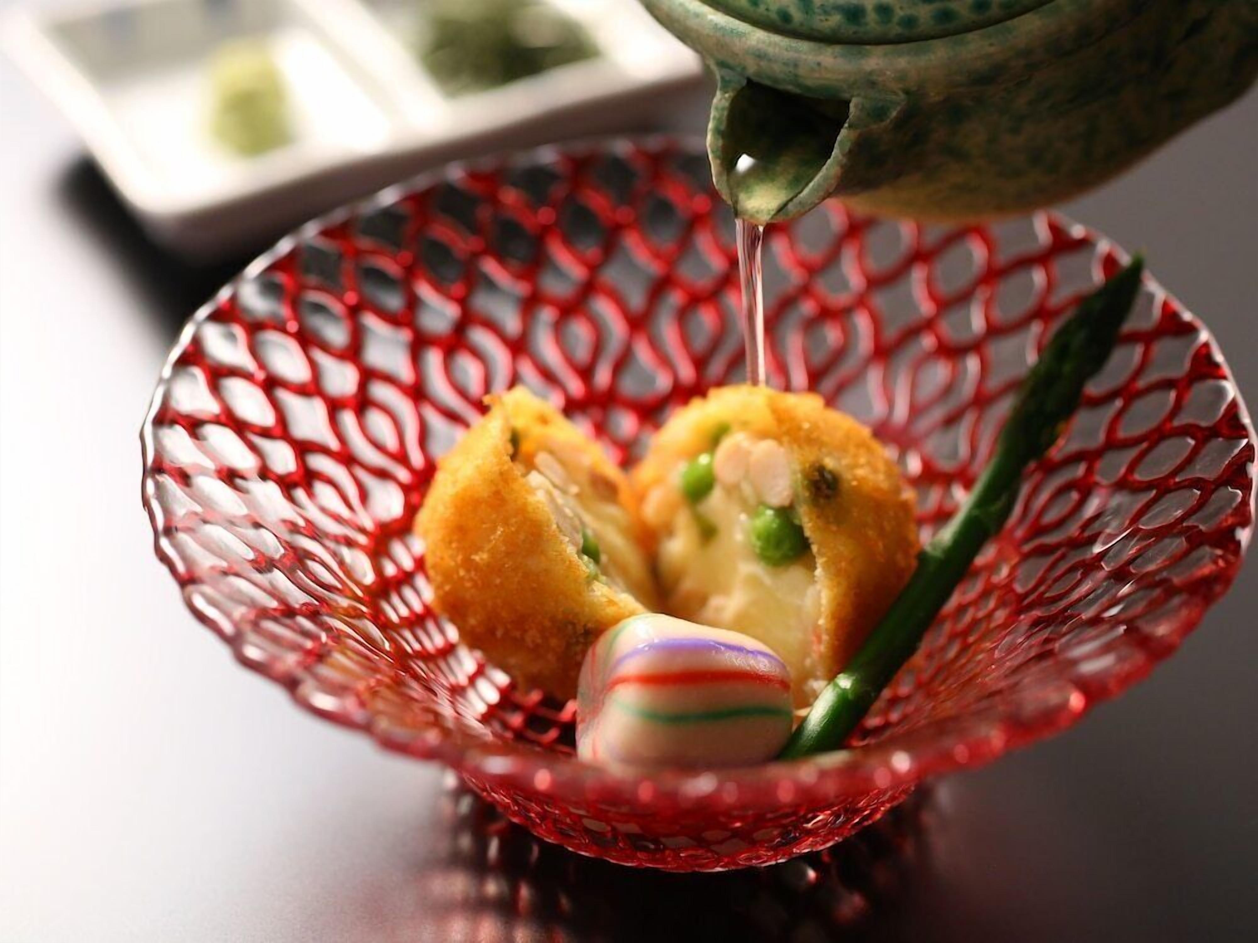 A red glass bowl containing a food item, a green vegetable, and a colorful object.