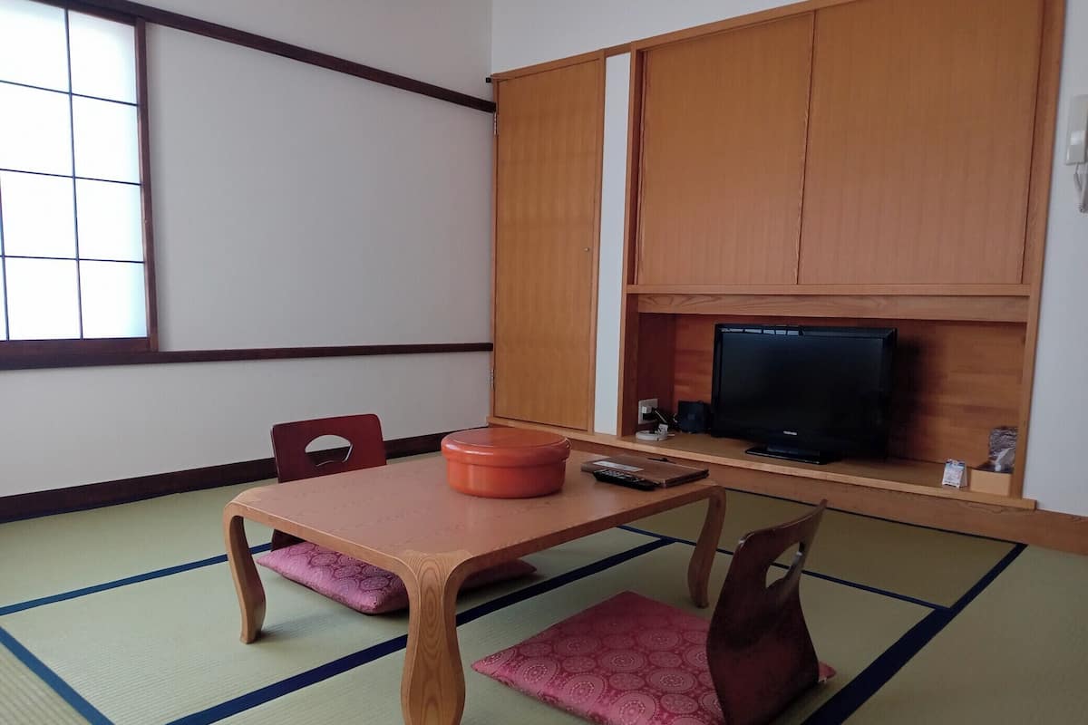 Perinteinen japanilainen huone, jossa on tatamimatto, matala pöytä, kaksi puutuolia, hyllyllä oleva televisio ja liukuovi.