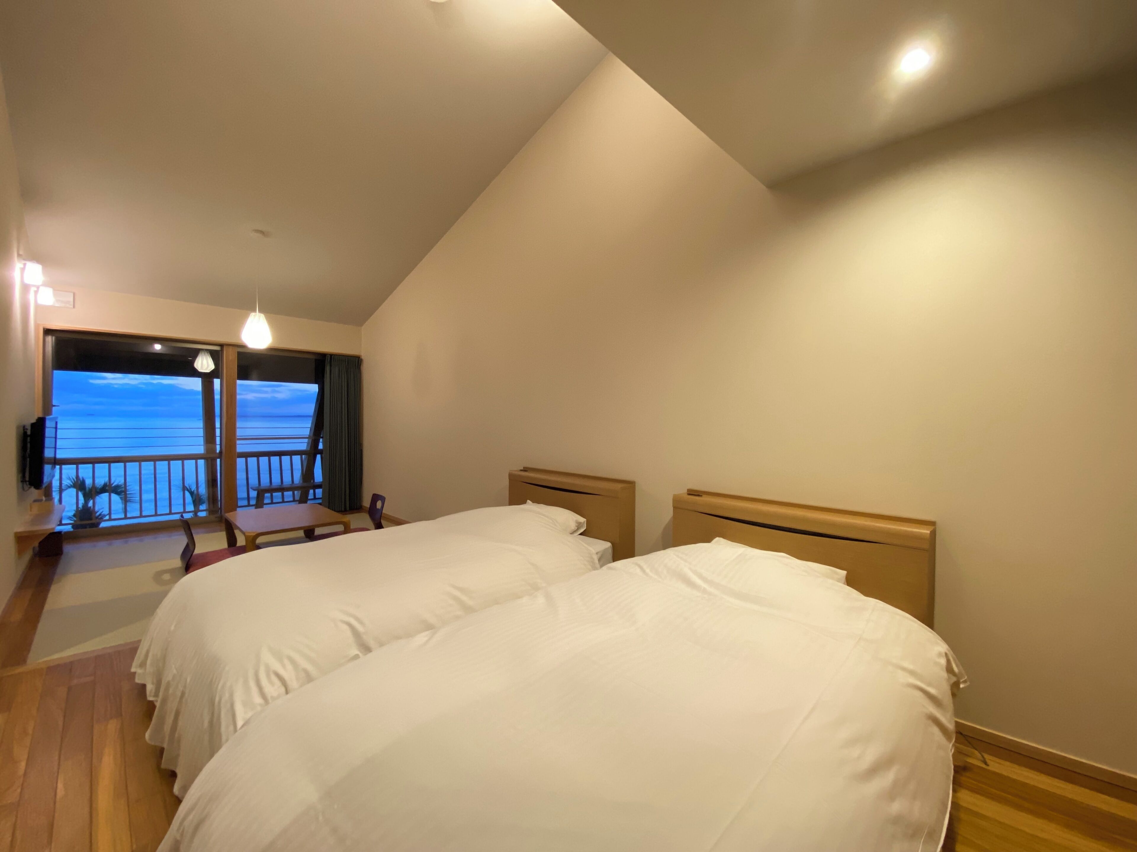 A hotel room with two beds, a balcony with a view of the sea, and a small table with chairs.