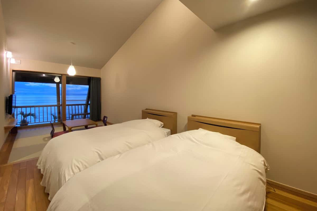 A hotel room with two beds, a balcony with a view of the sea, and a small table with chairs.