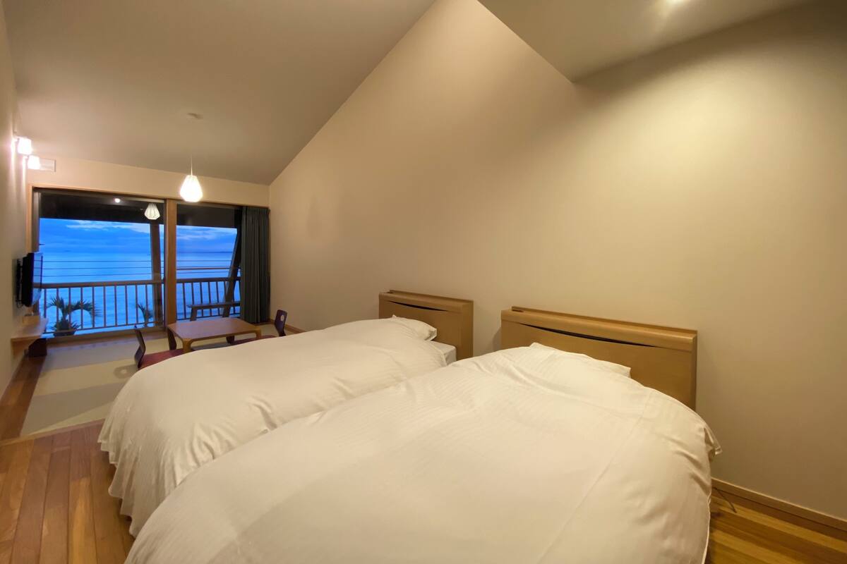 Hotellihuone, jossa on kaksi sänkyä, parveke, jolta on näkymä merelle, sekä pieni pöytä ja tuolit.